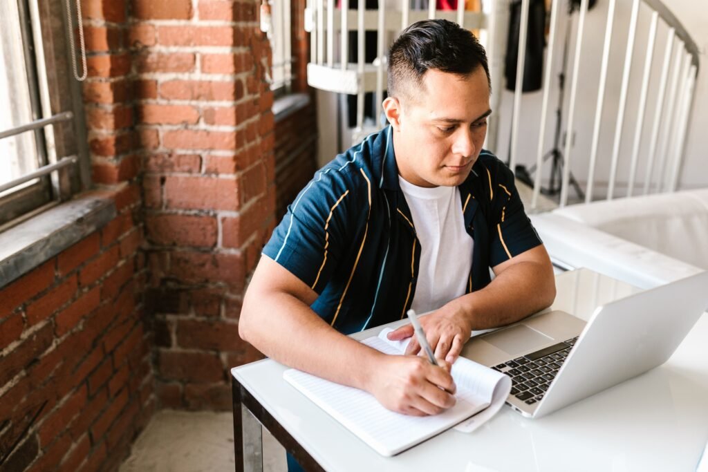 Man writing notes in notebook next to open laptop while learning a new skill online for free